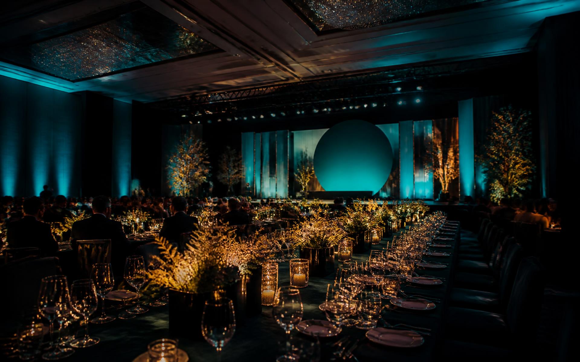 Corporate gala ballroom with staged backdrop, long banquet tables and dramatic lighting